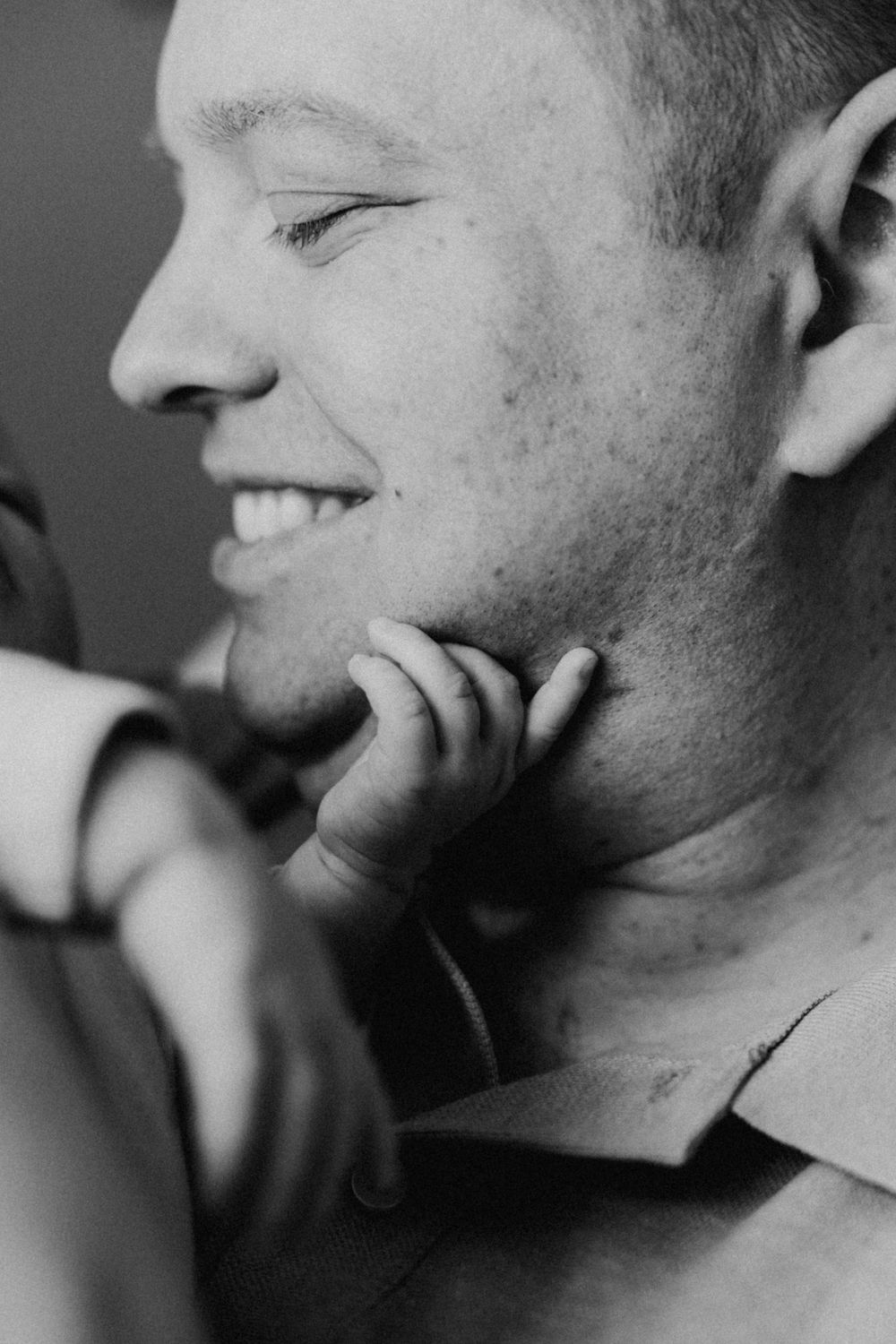 A black and white close-up portrait showing a candid smile in profile view.