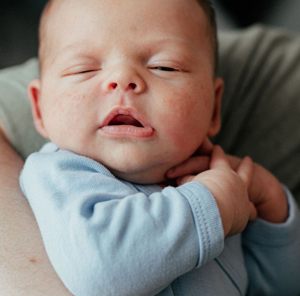 Sleeping newborn in light blue sleeper rests peacefully against soft fabric.