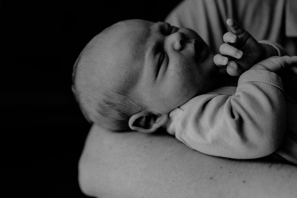 A sleeping baby in black and white rests peacefully against a soft surface with tiny fists curled up.
