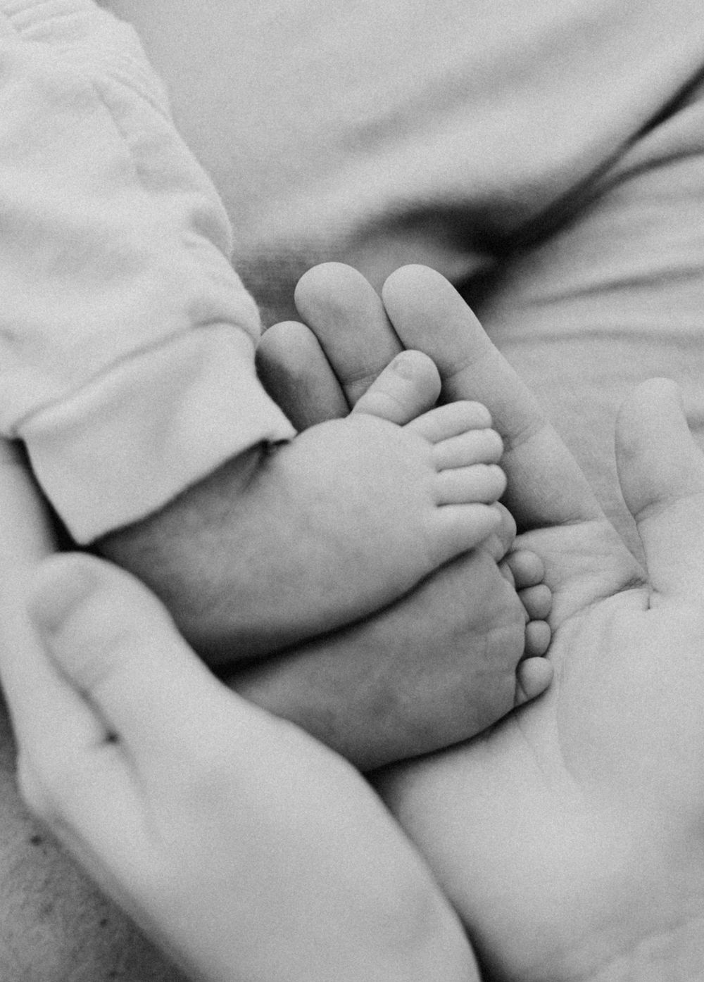 Close-up black and white image of tiny baby feet being gently held by adult hands.