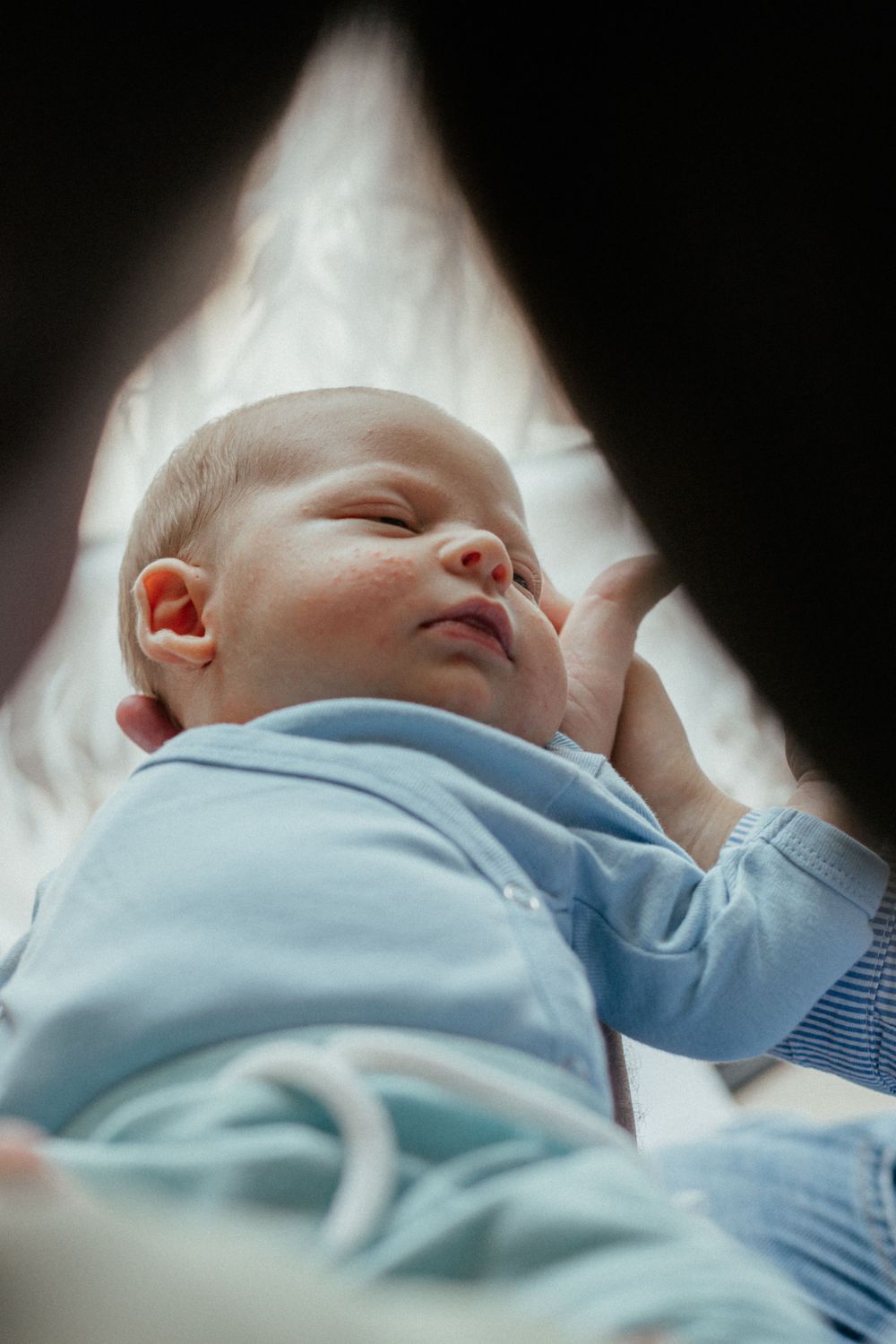A peaceful sleeping newborn baby wearing soft blue clothing rests against white bedding.