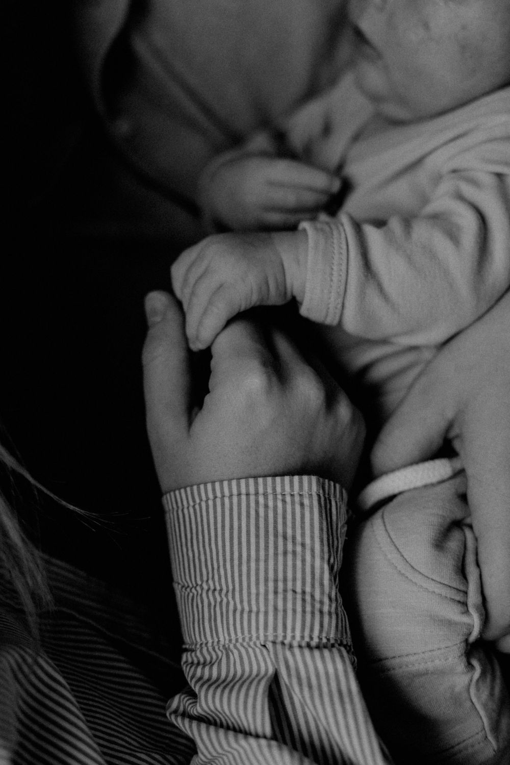 Black and white closeup of adult hands tenderly holding tiny infant feet in gentle embrace.