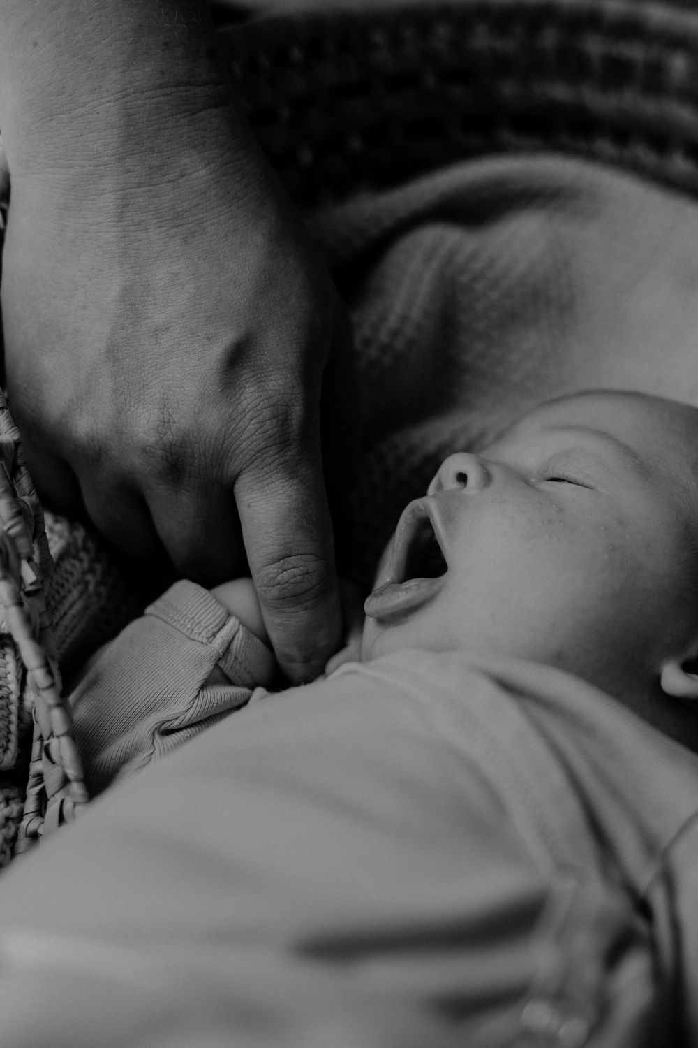 Close-up black and white photo of baby yawning while lying down.