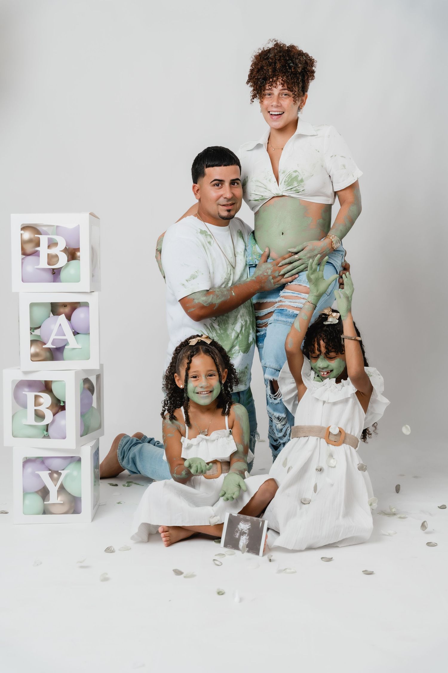 Family maternity photoshoot with decorative baby blocks and white theme.
