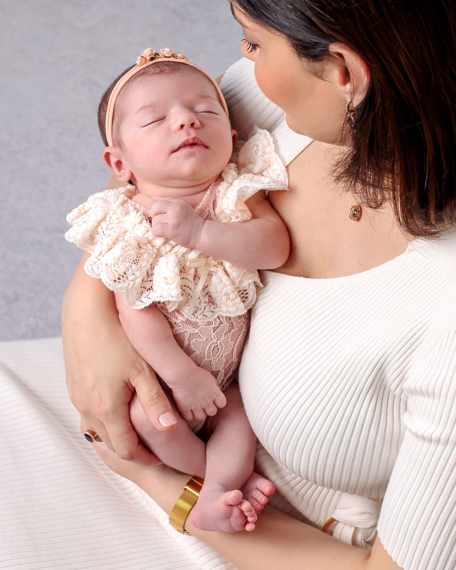 Close up over the shoulder portrait, mother gazes lovingly at newborn baby girl sleeping peacefully in her arms.