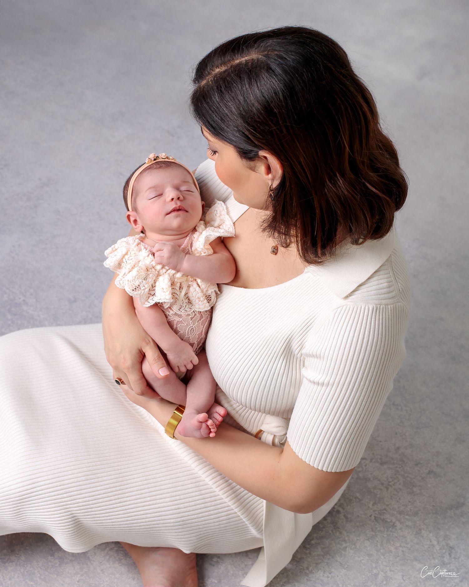 Newborn portrait Birdseye view of mother sitting on the floor holding her newborn daughter. Newborn girl in peach lace romper and headband