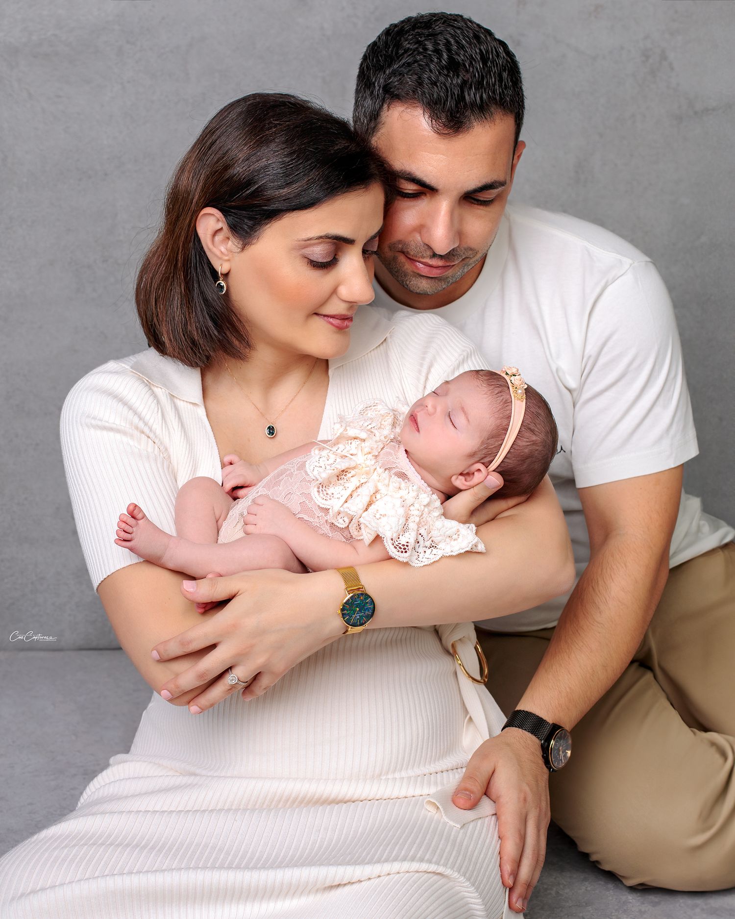 Close up of a mum and dad huddled together sitting on floor lovingly looking at their newborn baby girl by Caz Captures Sydney Photographer