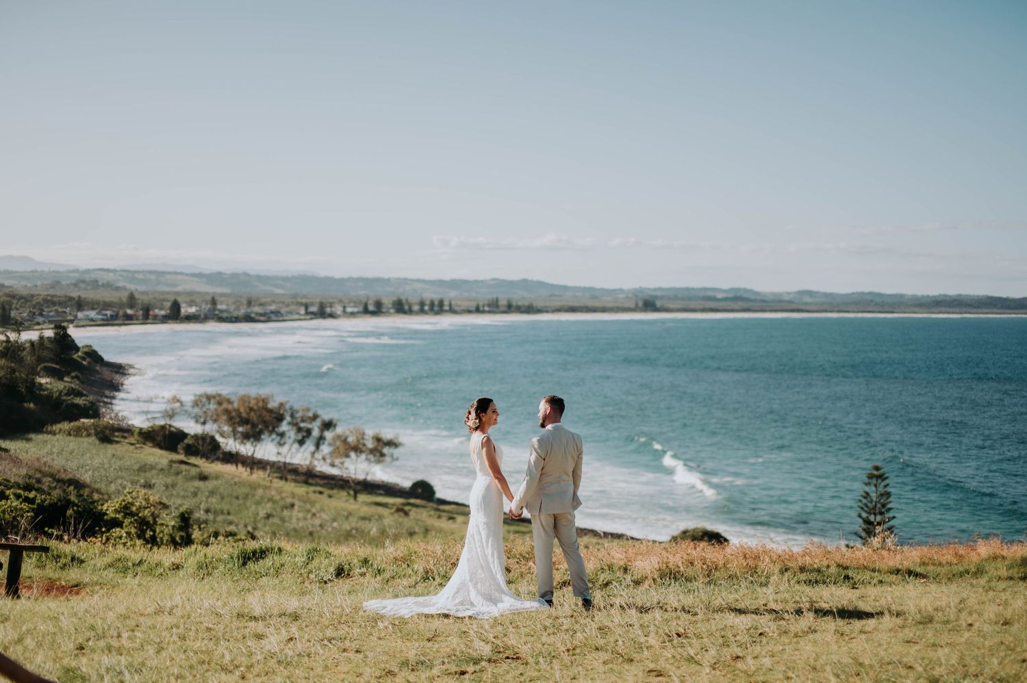 Scenic coastal wedding portrait with couple overlooking ocean bay view.