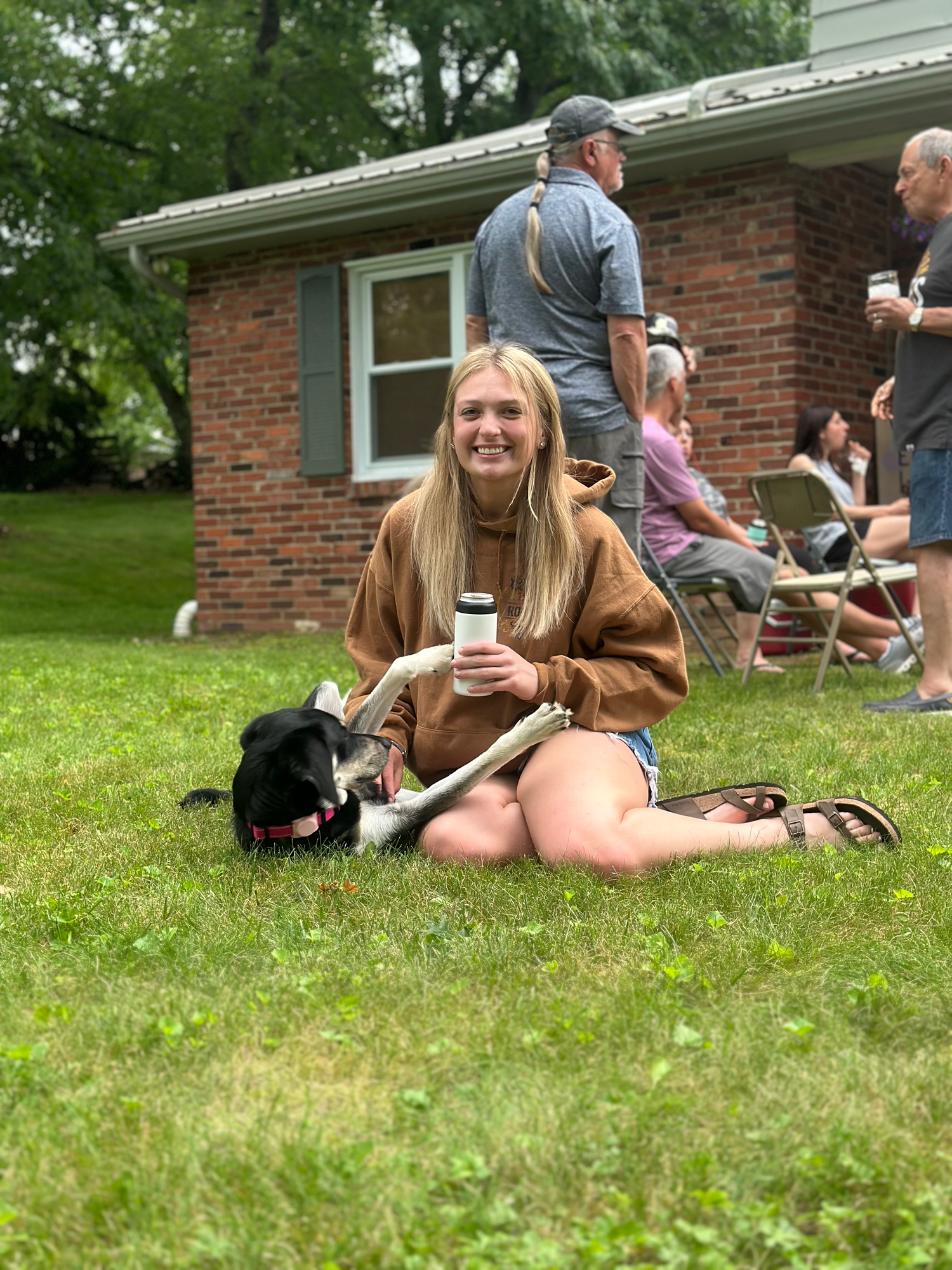 A casual backyard gathering with people relaxing on the lawn near a brick house.