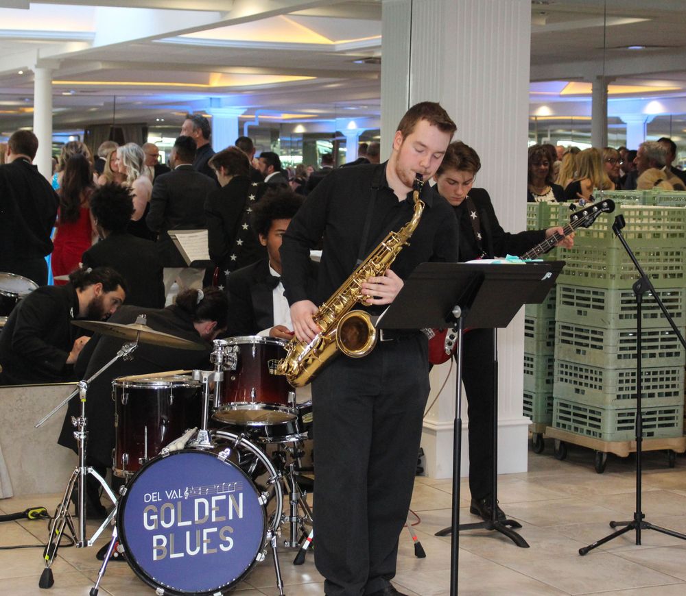 A saxophone player performs with a jazz band called Golden Blues at an indoor venue.