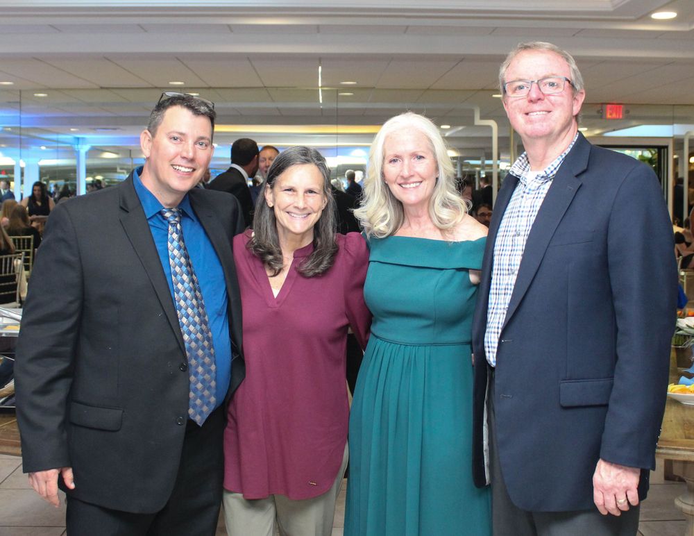 Four attendees pose together at a formal event with the men in suits and women in evening wear.