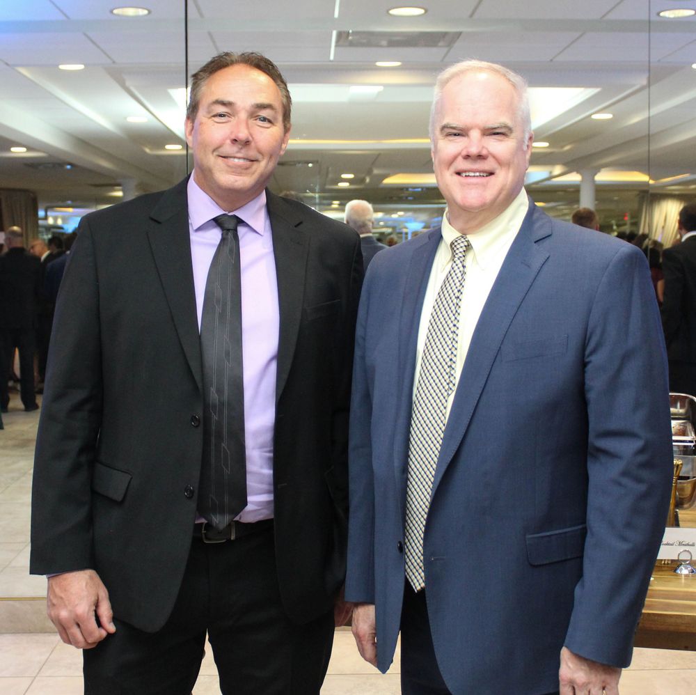 Two professionals in business suits stand together at a corporate event.