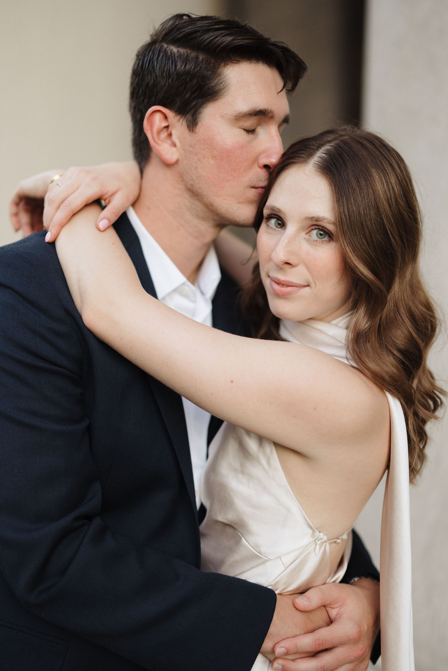 A close-up romantic portrait of a couple in formal attire against a neutral background.
