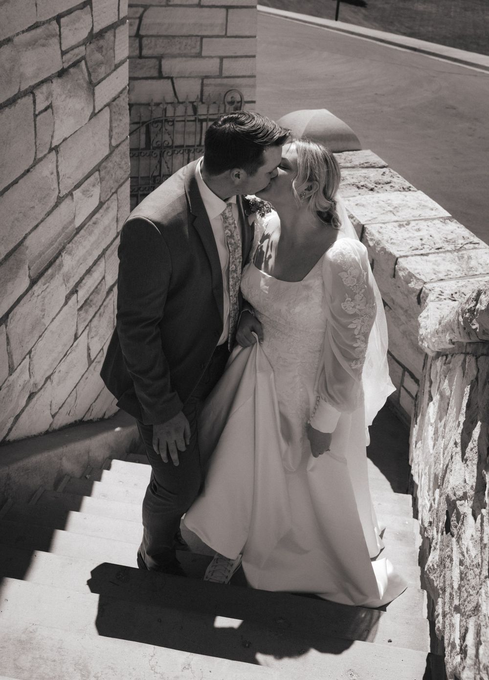 Black and white photo of bride and groom sharing a kiss on stone steps at their wedding venue.