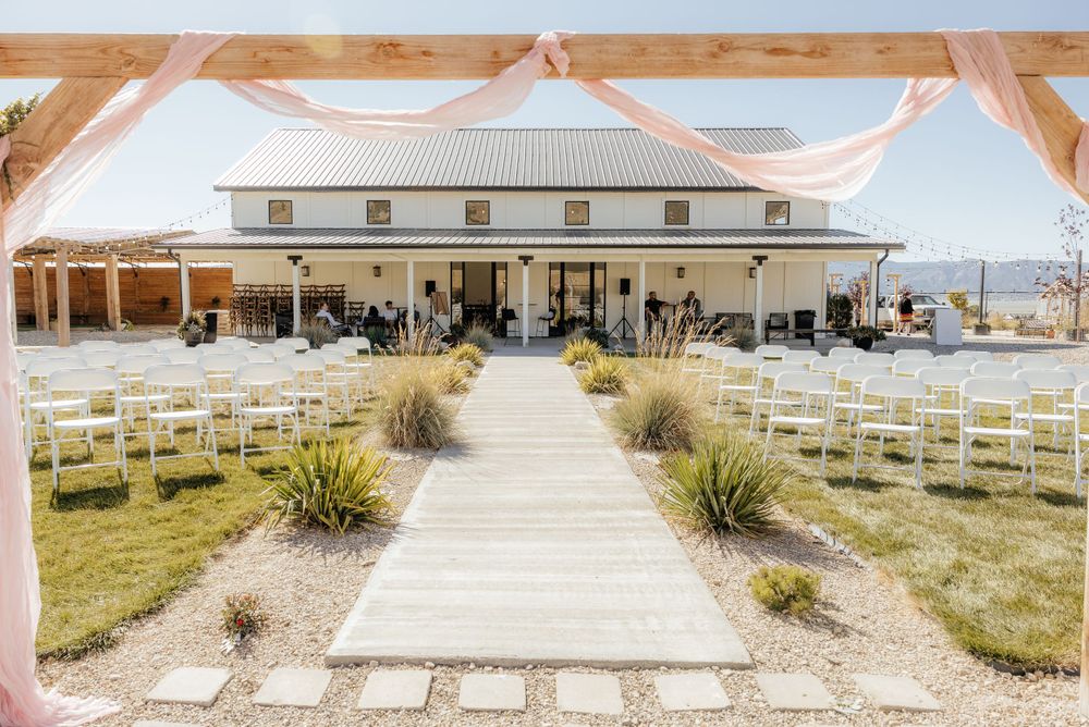 Elegant outdoor wedding ceremony setup with white chairs lining an aisle at a white barn venue.