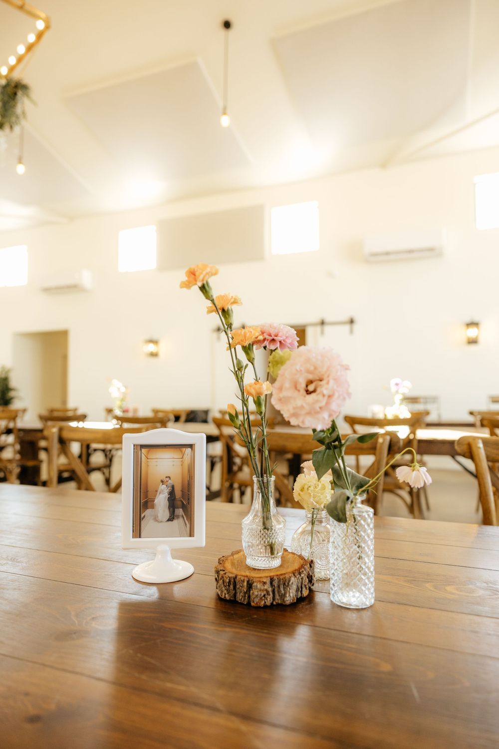 Rustic wedding reception table with bud vases of peach flowers and a framed couple photo on wood slice.