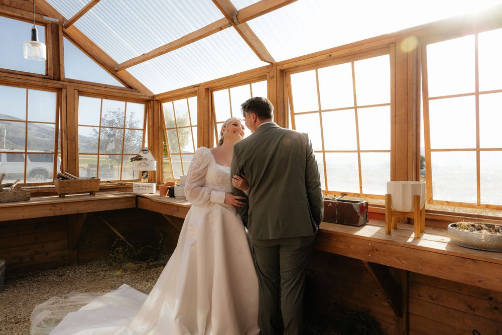Bride and groom share an intimate moment inside a sunlit rustic wooden greenhouse on their wedding day.