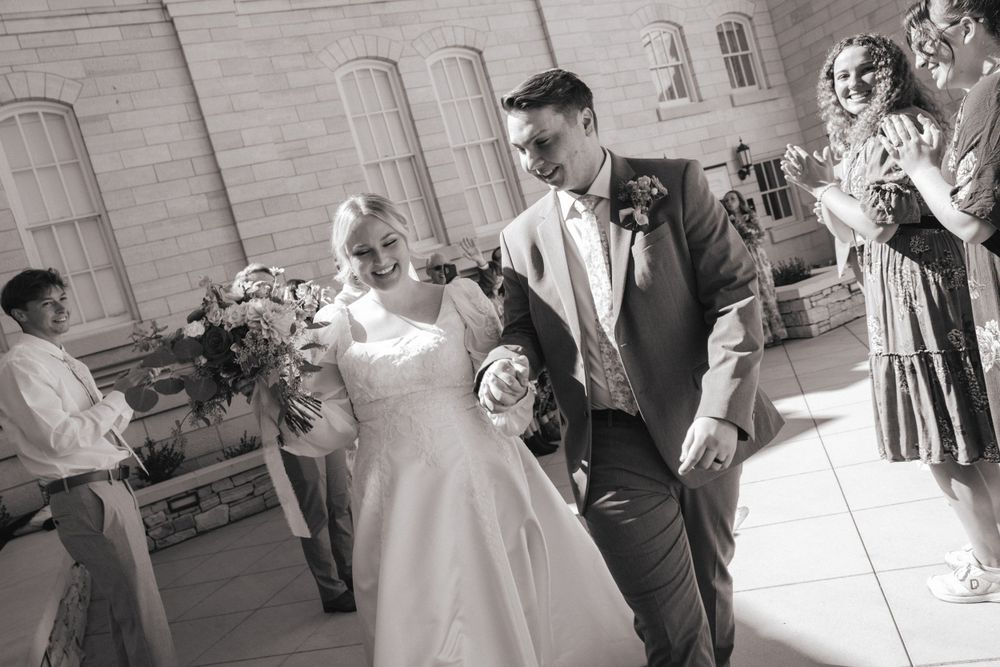 Bride and groom joyfully exit their wedding ceremony as guests celebrate outside a classic stone building.