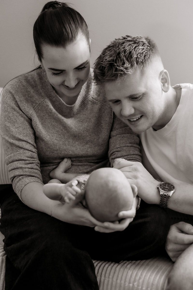 Svart-hvitt bilde av en mamma og pappa som ser kjærlig på babyen sin.