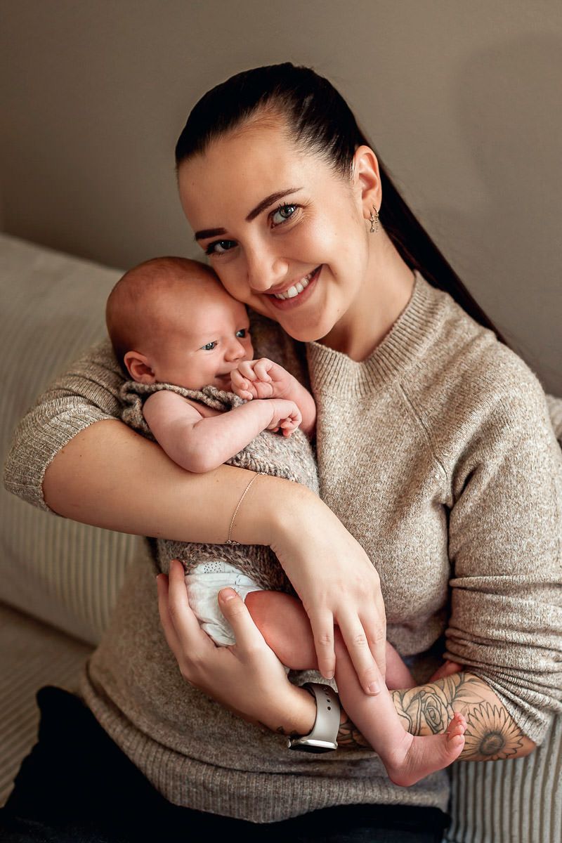 Nybakt mor holder babyen sin og smiler til kamera.