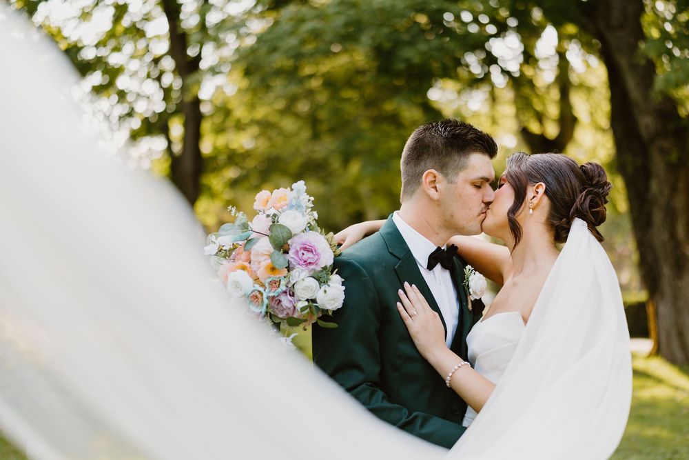 A romantic wedding couple shares a tender kiss in a sun-dappled garden setting with golden bokeh lighting.