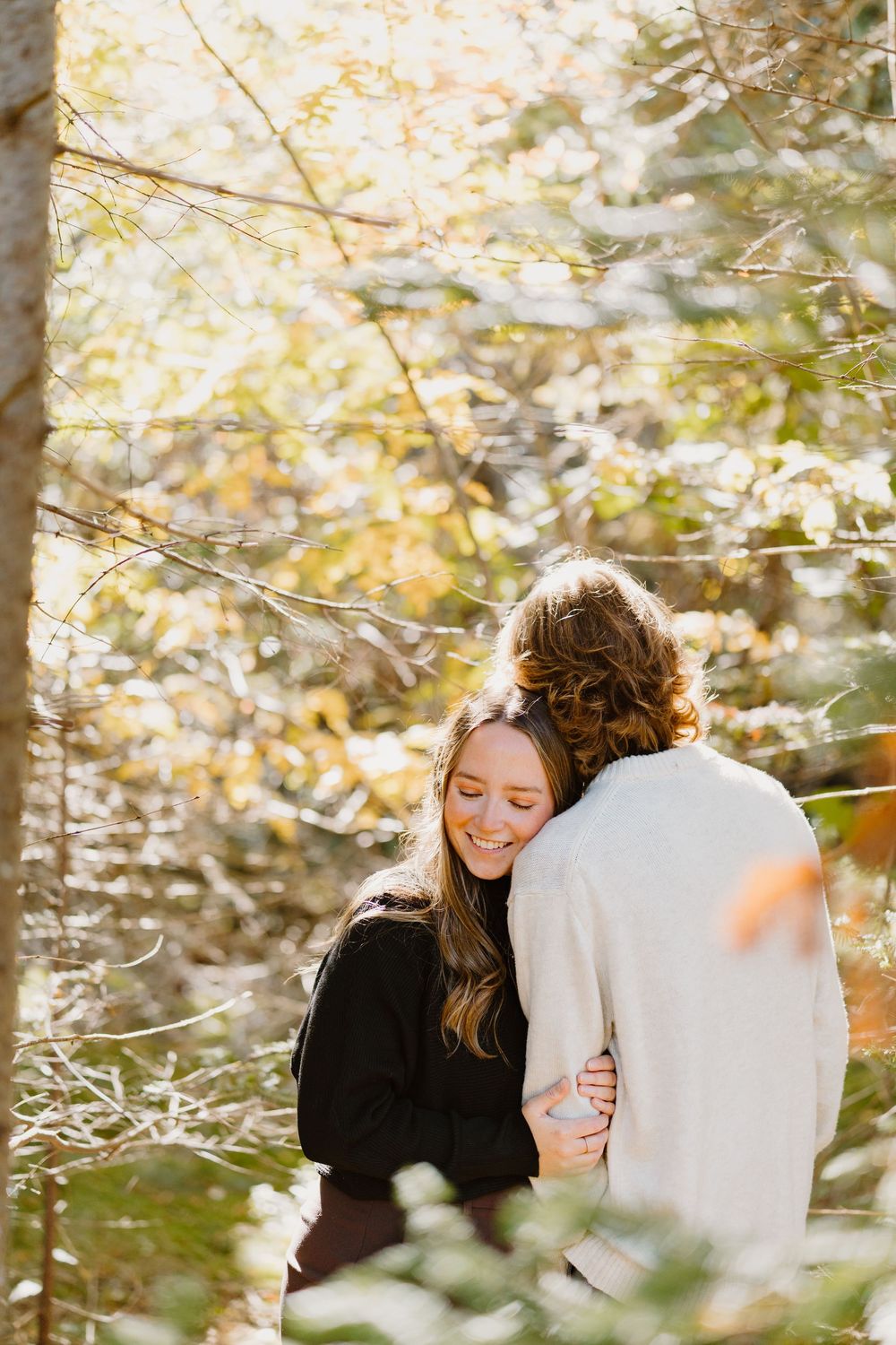 Couple sharing intimate moment outdoors in autumn forest with sunlit bokeh effect in background.