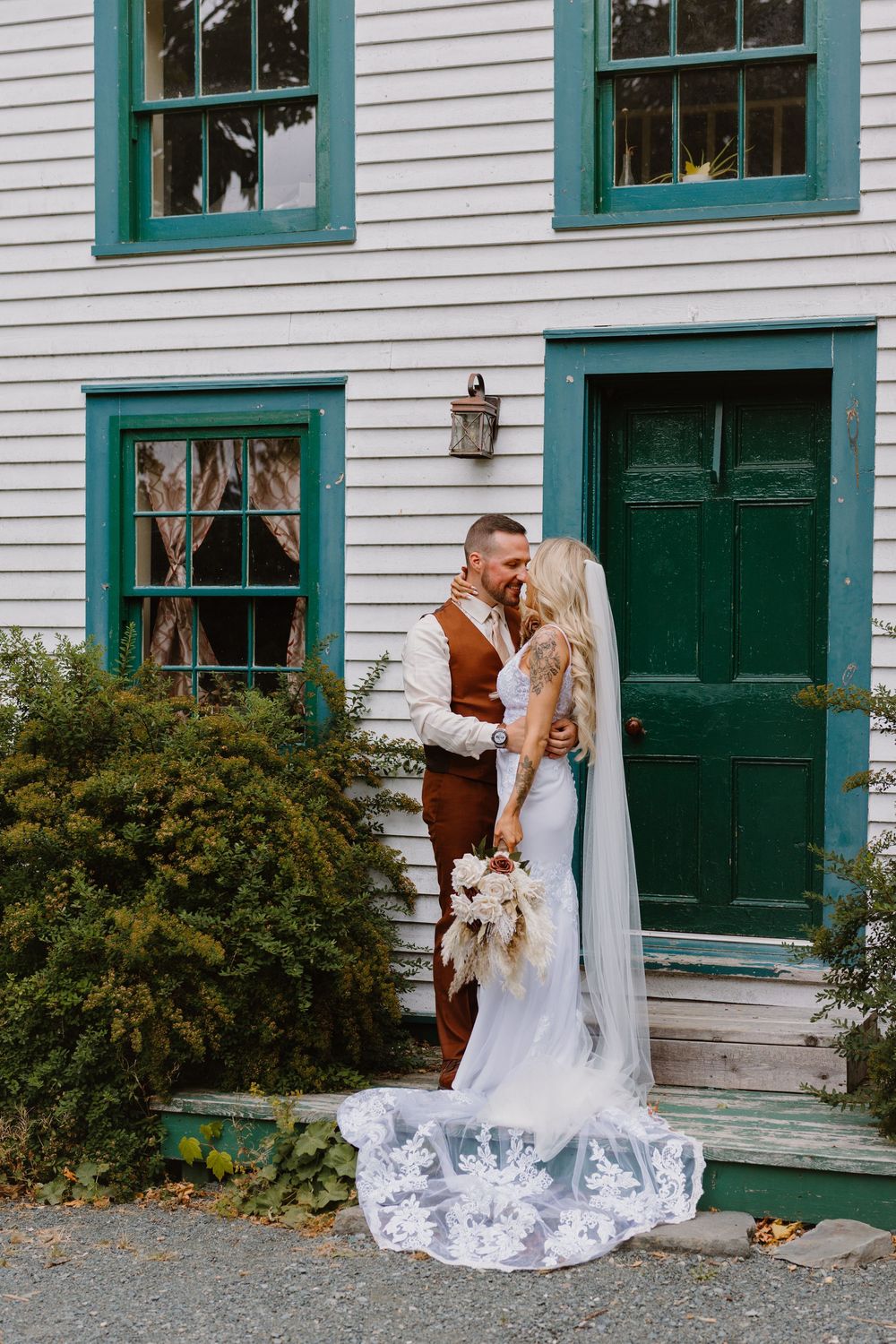 A romantic wedding couple shares intimate moments in front of a white building with green trim and doors.