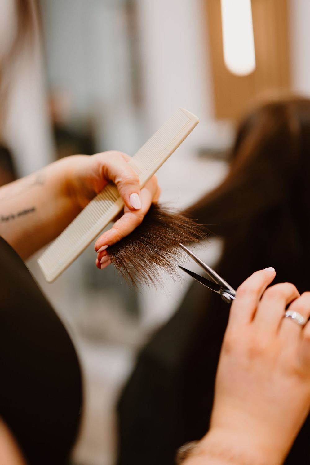 Close-up of a hairstylist trimming dark hair ends with scissors and a comb in a professional salon.
