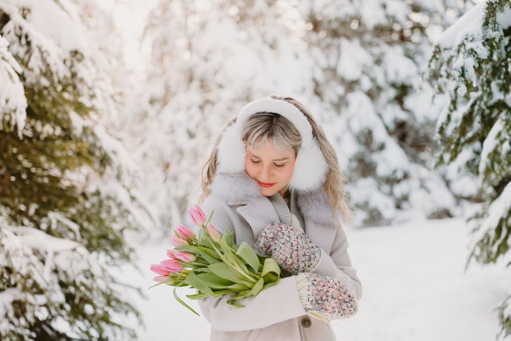A winter scene with pink tulips in the snow surrounded by evergreen trees and frost-covered branches.