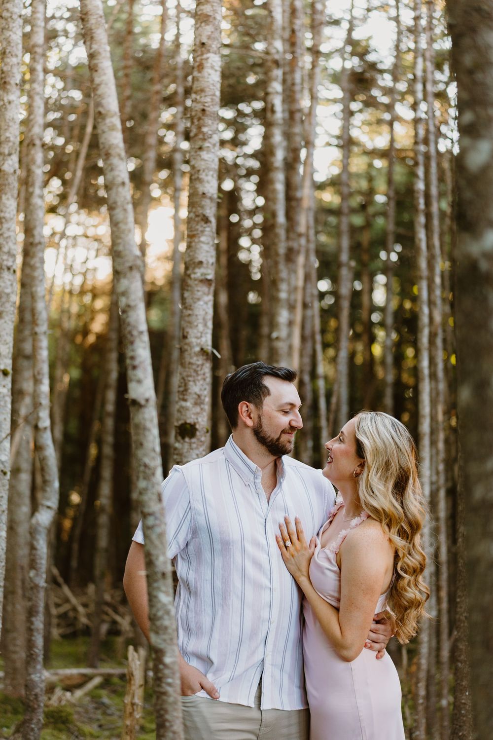 Romantic couple embraces in a sunlit birch forest during engagement photo session at sunset.
