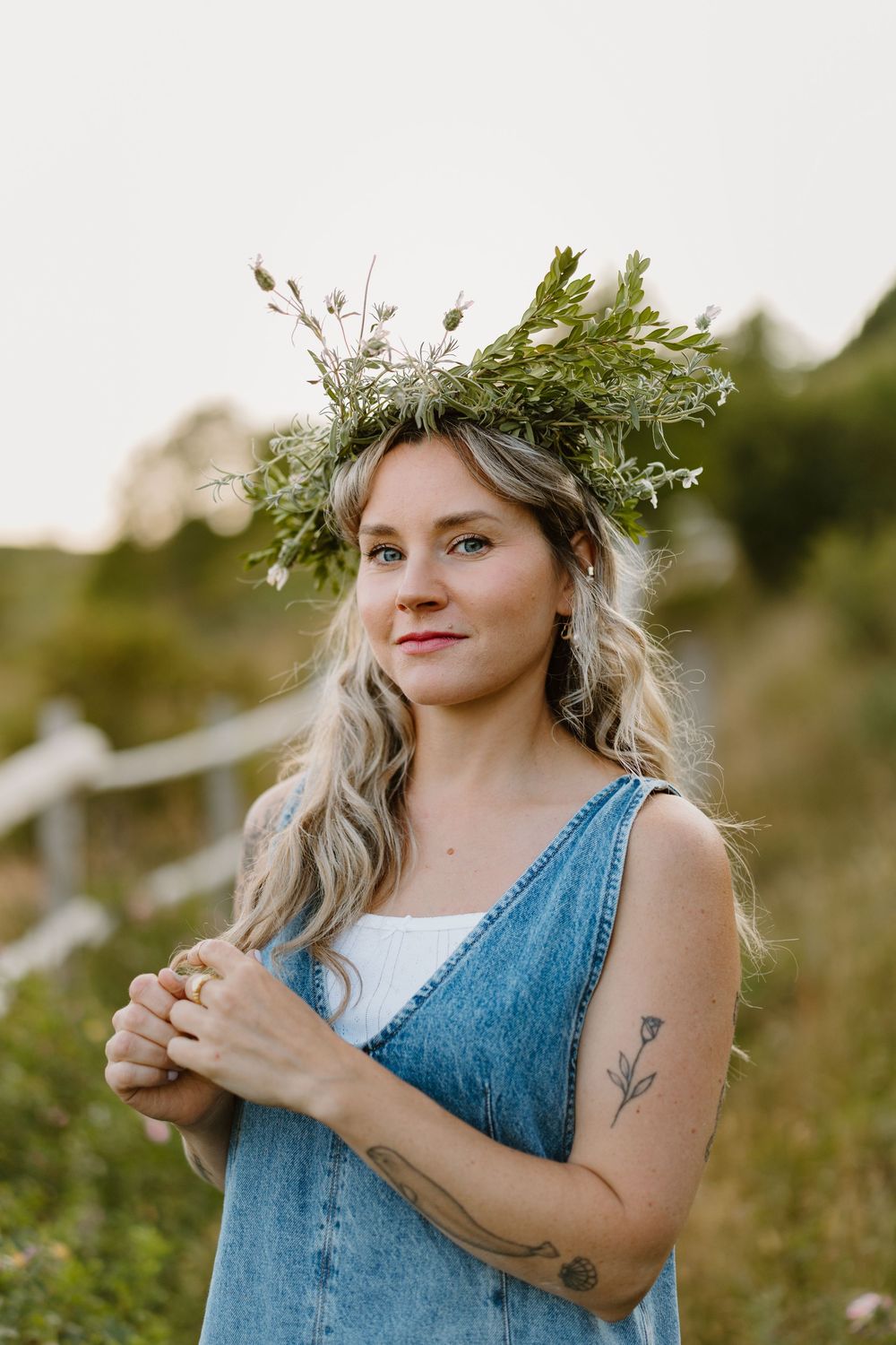 Someone wearing a blue denim dress and floral crown stands in a sun-lit meadow.