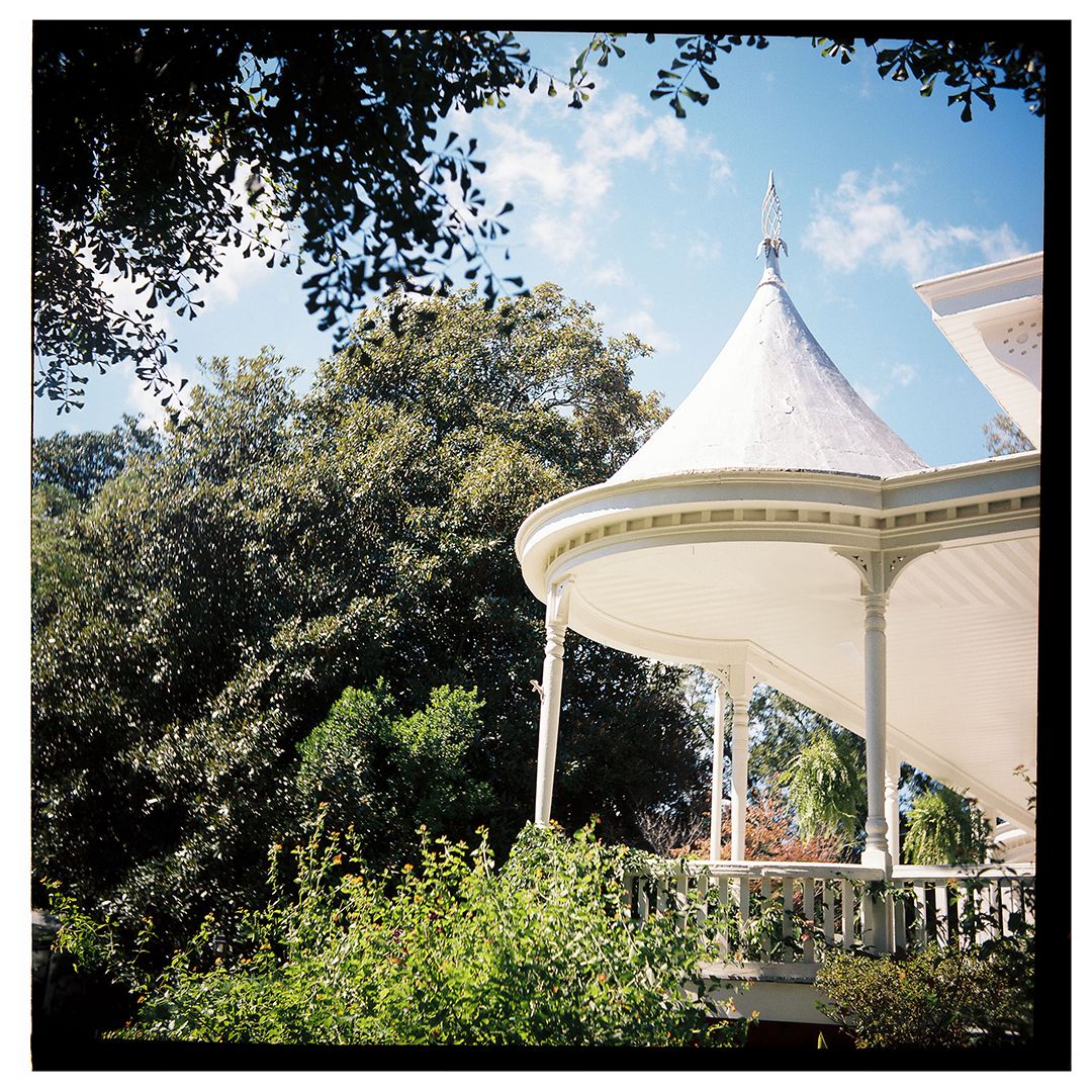 White gazebo structures with pointed roofs stand in a lush garden setting on a sunny day.
