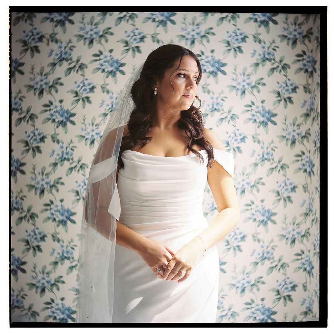 Elegant bridal portrait against blue floral wallpaper in soft natural lighting.