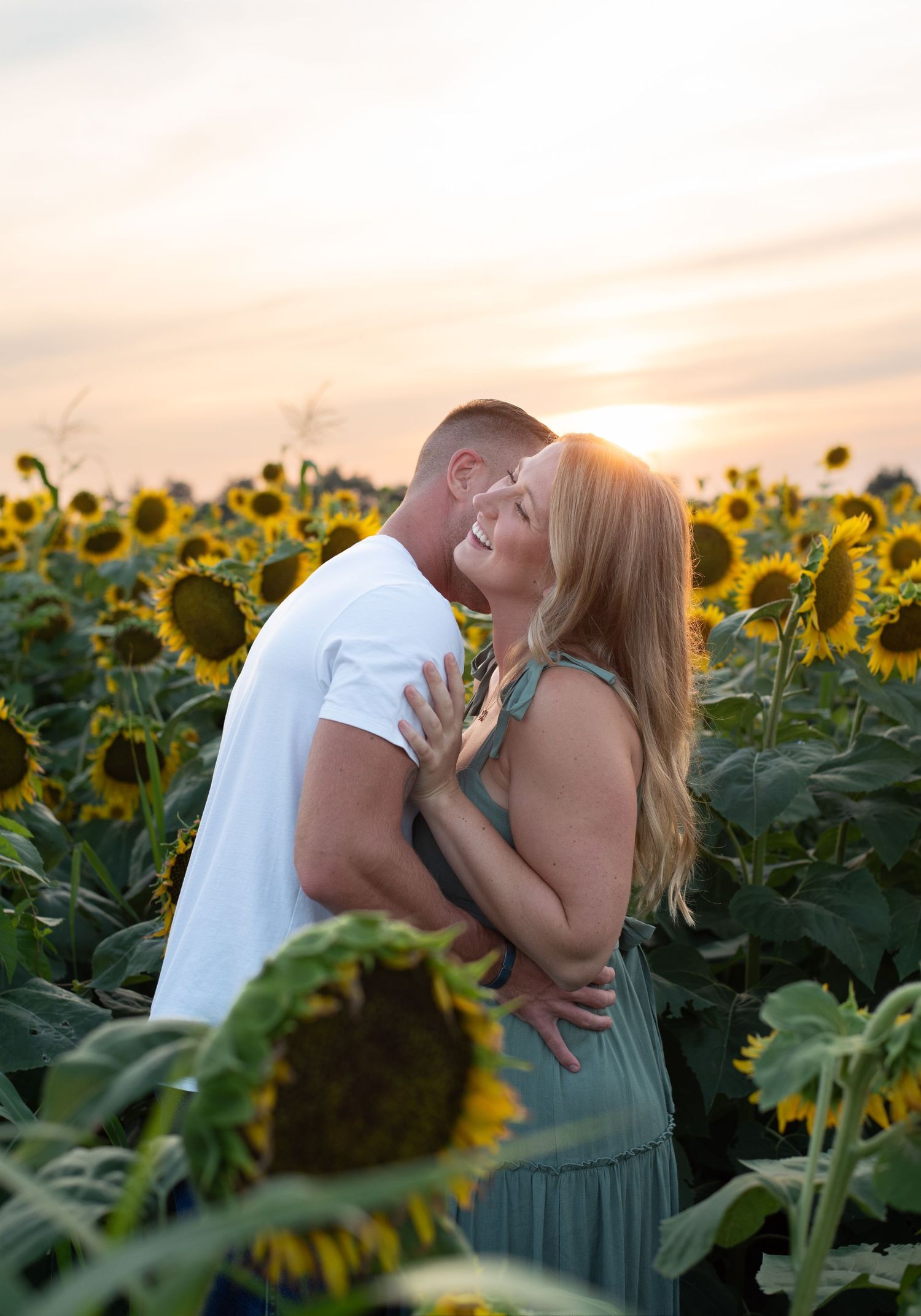 Romantic couple embracing in sunflower field during golden hour sunset.