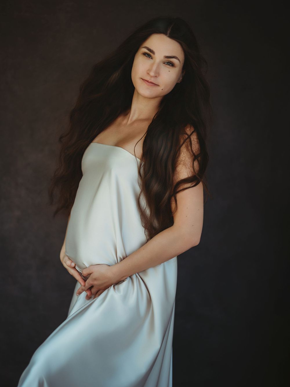 A woman in a white dress poses gracefully against a dark background in a series of artistic portrait photographs - maternity photography
