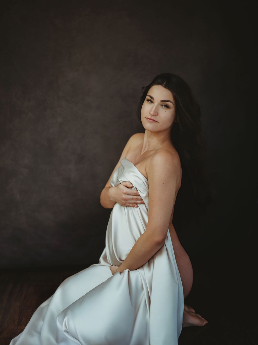 Artistic boudoir portrait series featuring a figure draped in white fabric against a dark moody background - maternity photography Bellevue