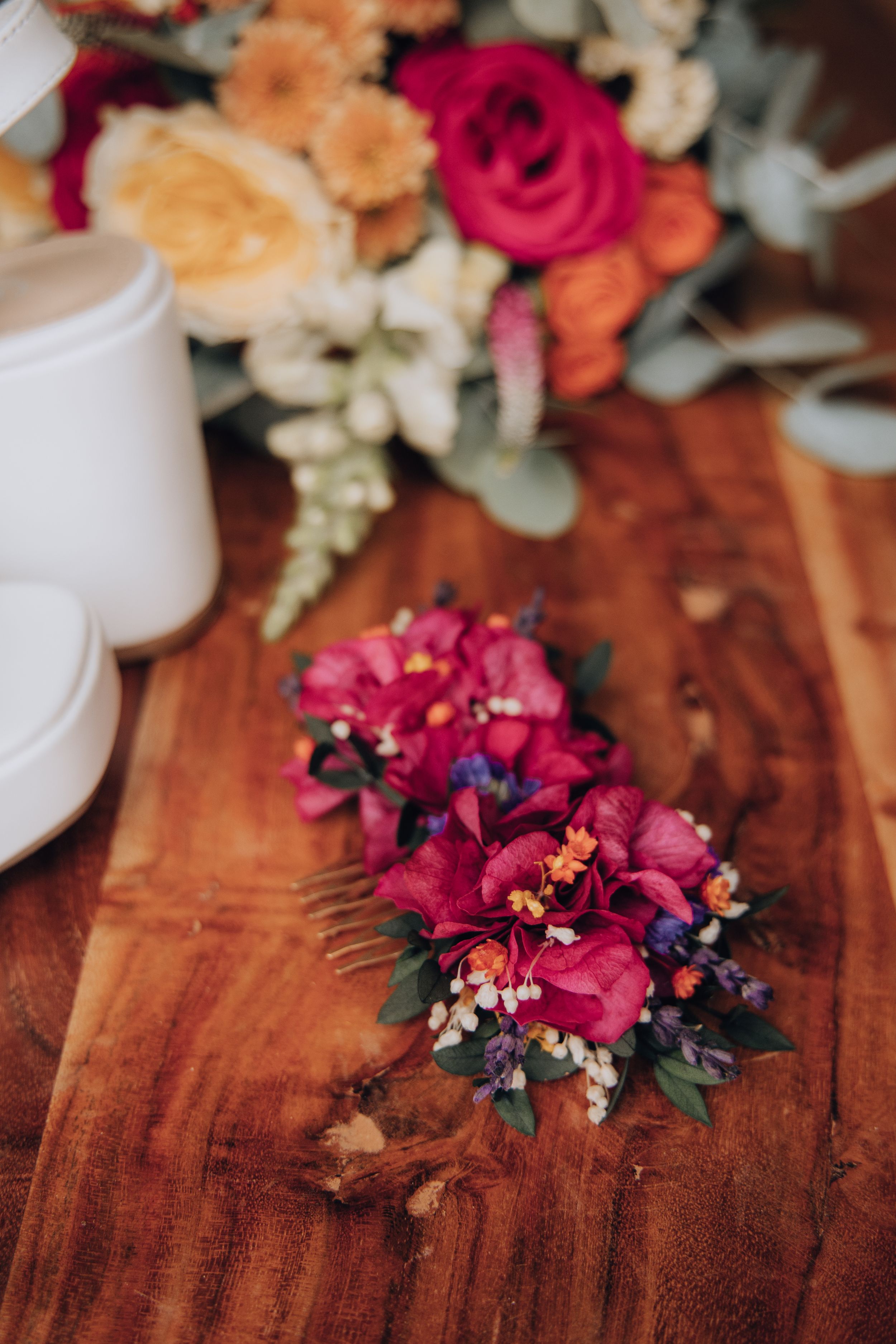 Colorful bridal hair comb with pink flowers and greenery on a wooden surface.