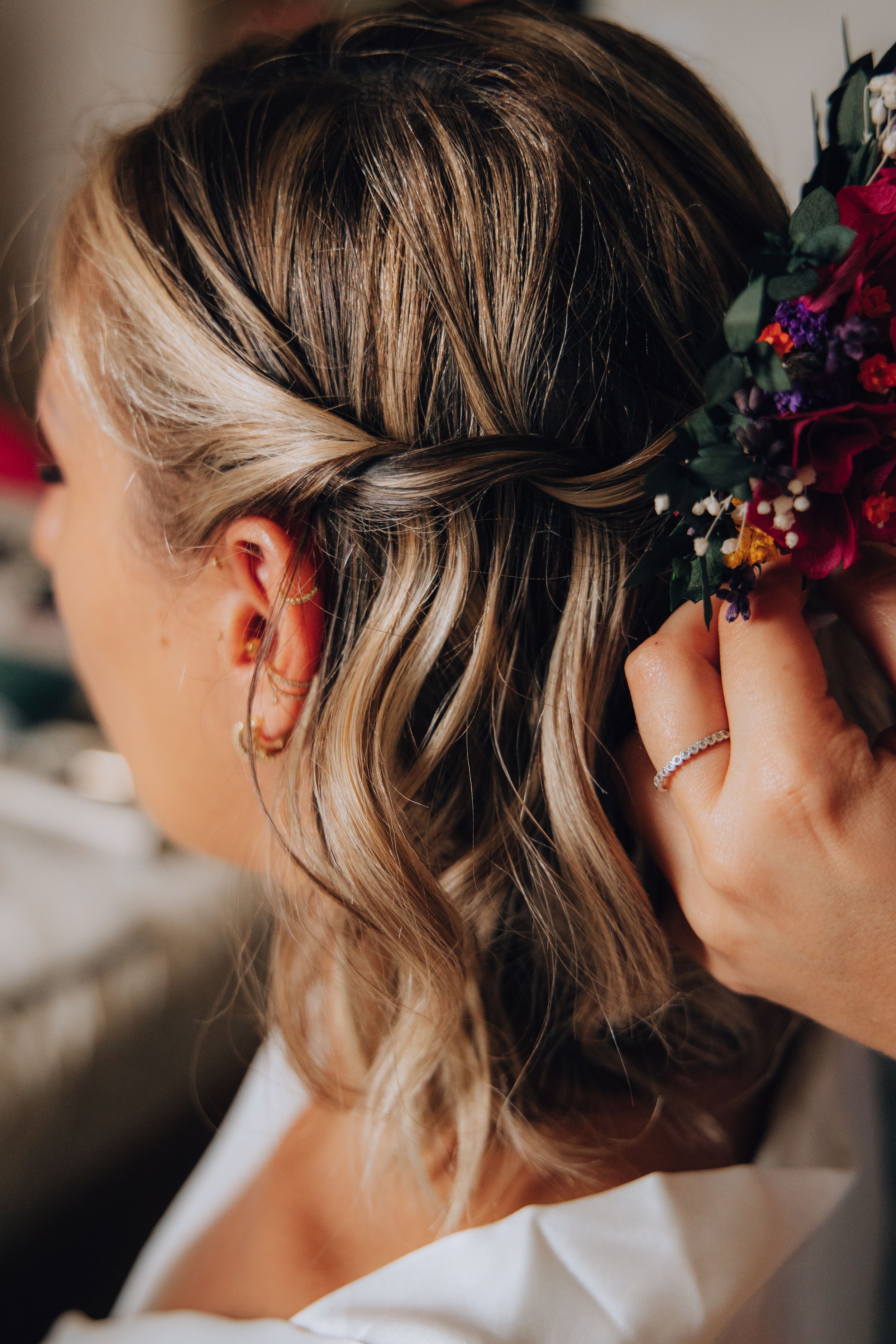 Hairstylist placing a colorful floral hair comb into bride's half-up hairstyle.