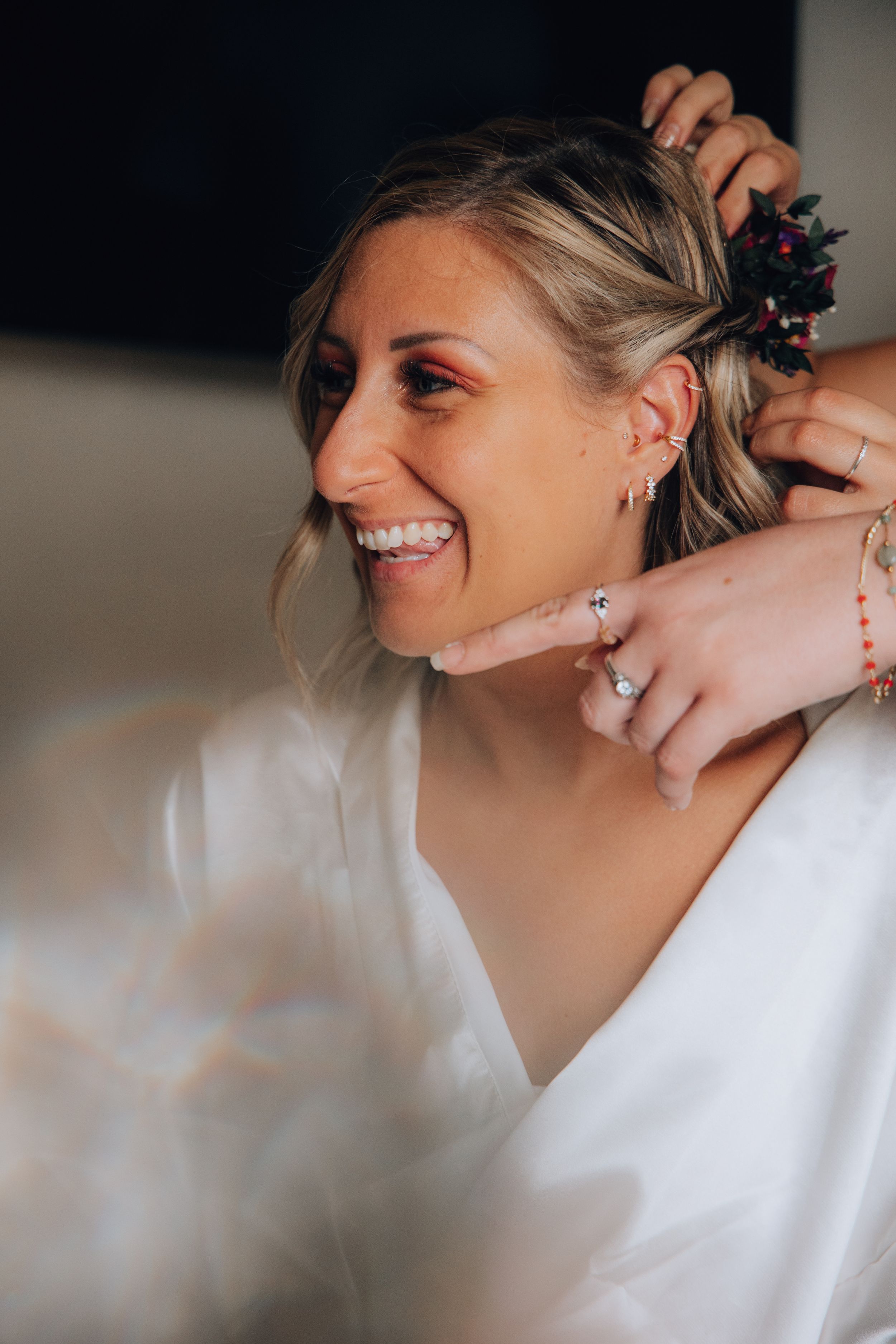 Smiling bride having floral hair accessory placed in her hair while getting ready.