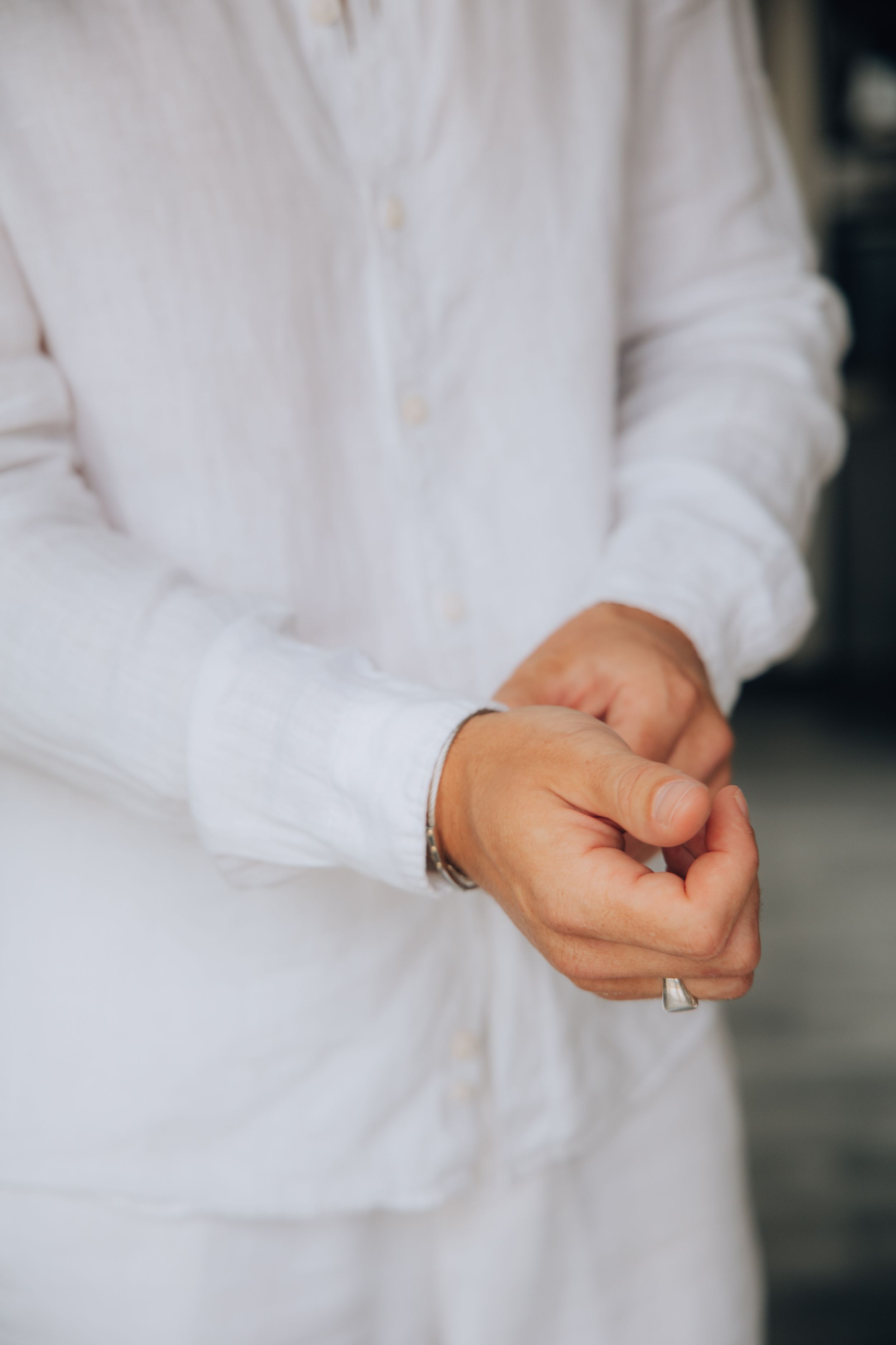 Groom in white linen shirt fastening his cufflinks while preparing for his wedding day.