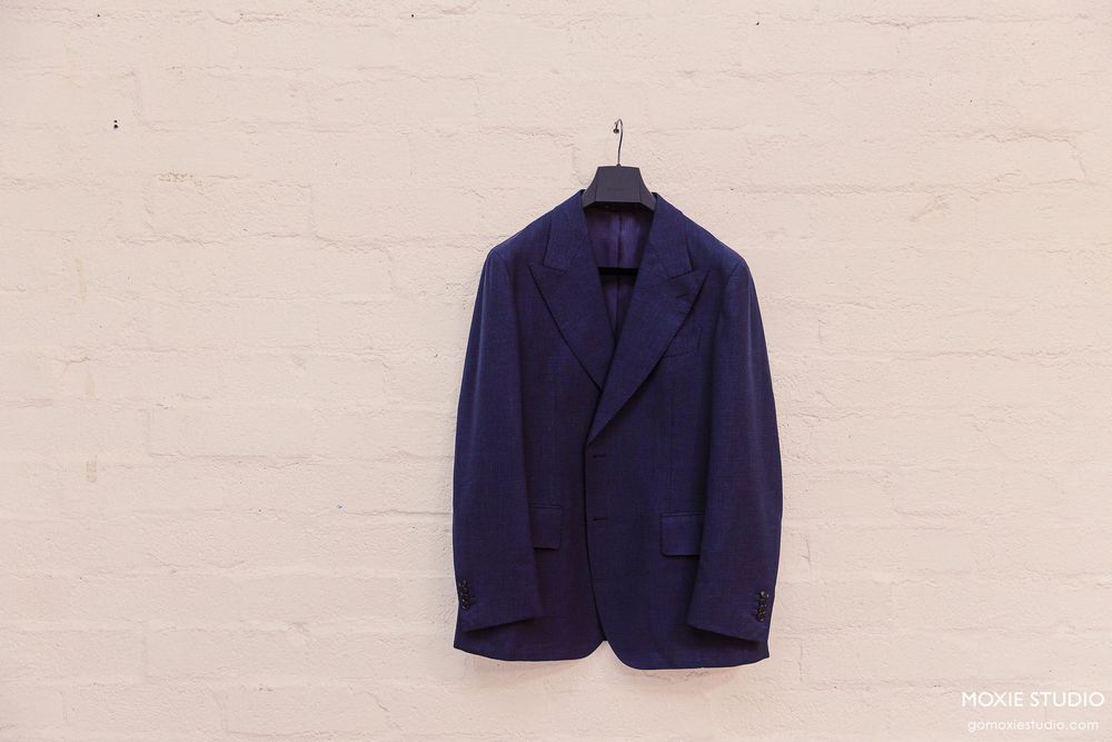 Row of navy blue and beige formal suit jackets hanging on display against white background.