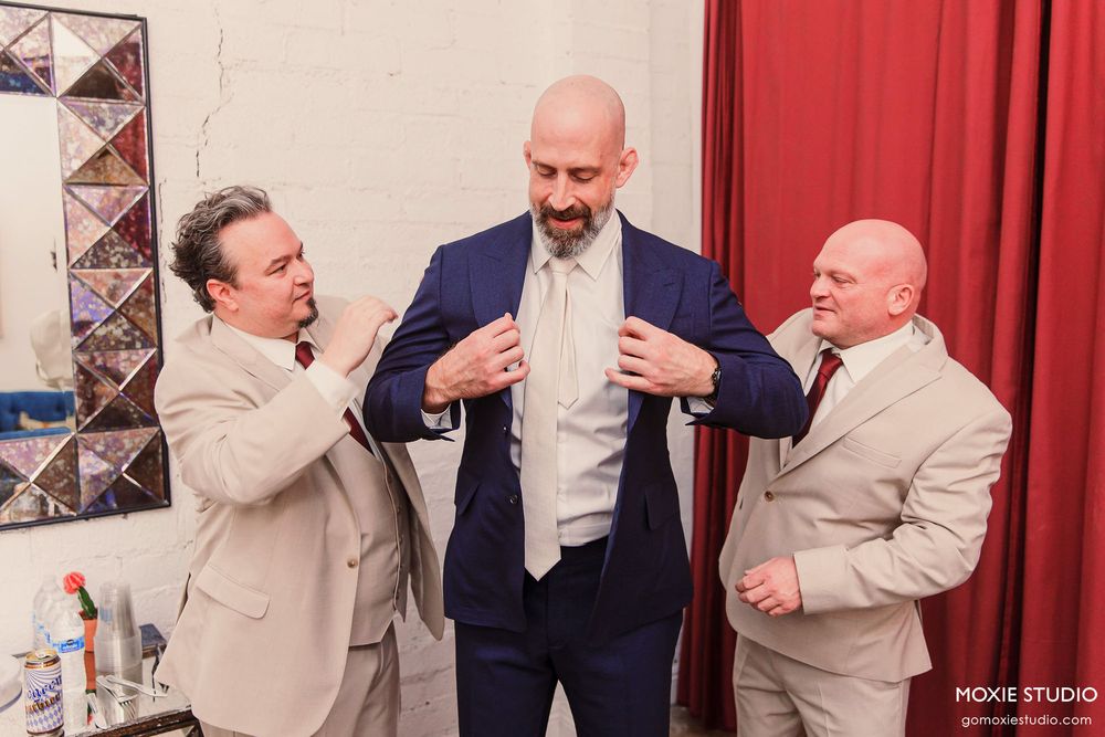 Groomsmen in light colored suits sharing candid moments and laughing together at a wedding.