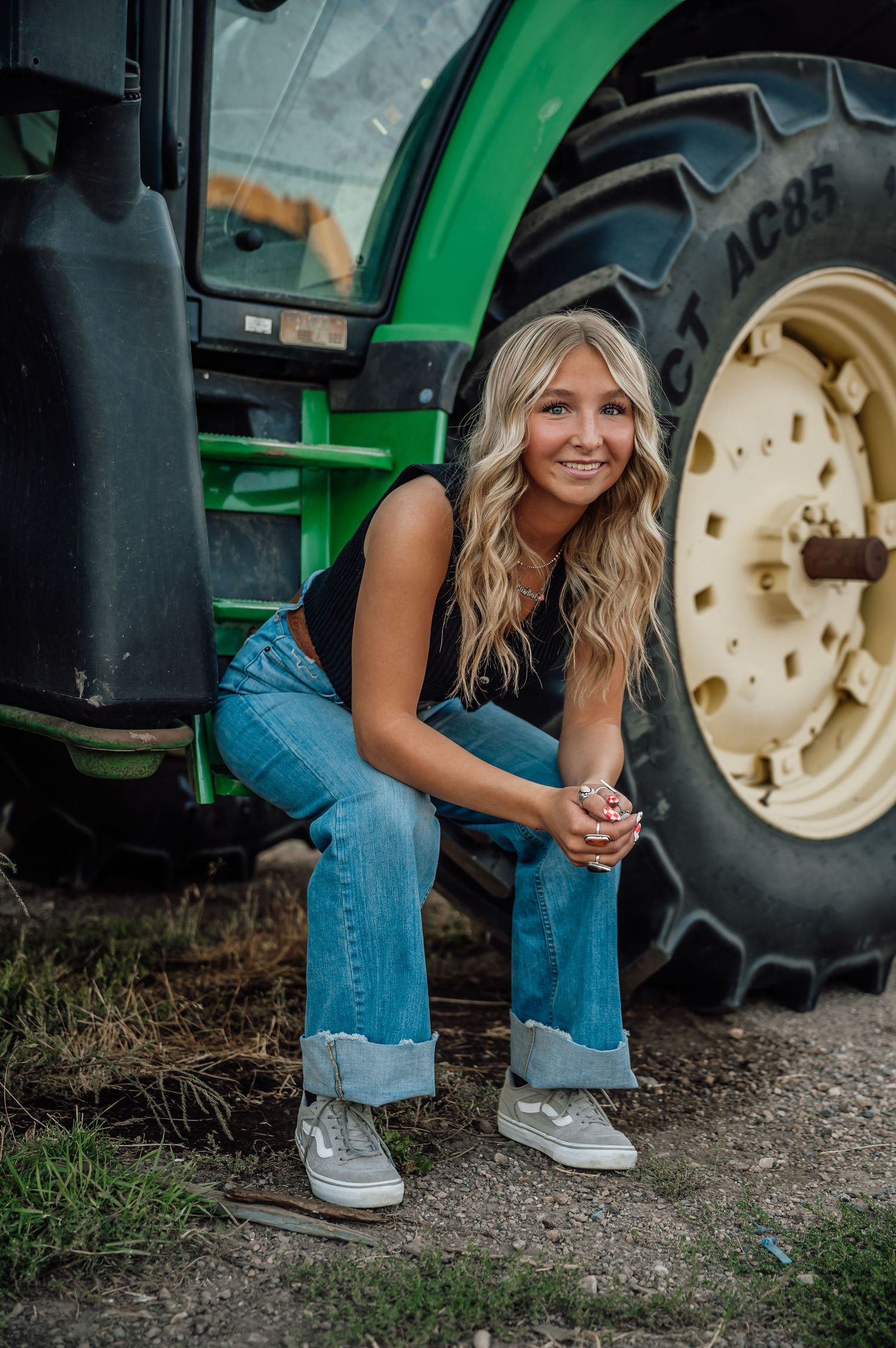 Person in denim crouching next to a green John Deere tractor.