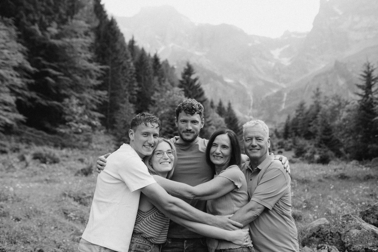 Group of friends embracing in a scenic mountain landscape with forest and peaks in background.