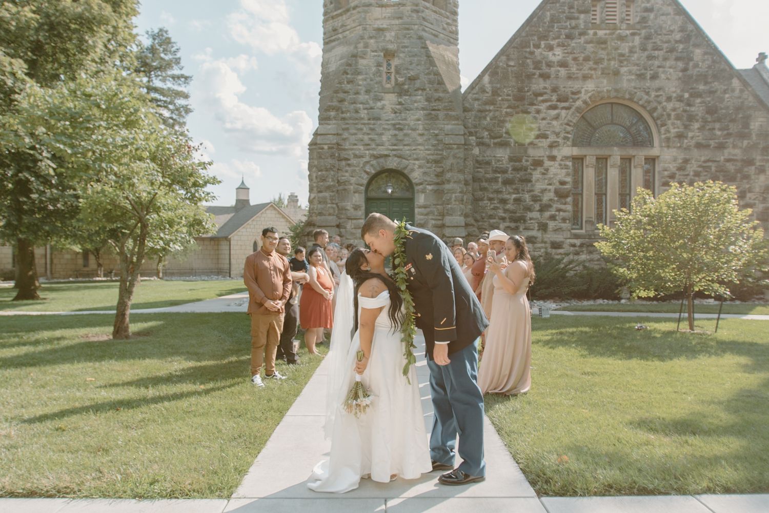 A couple in military dress and white wedding attire stand together in a bright indoor setting.