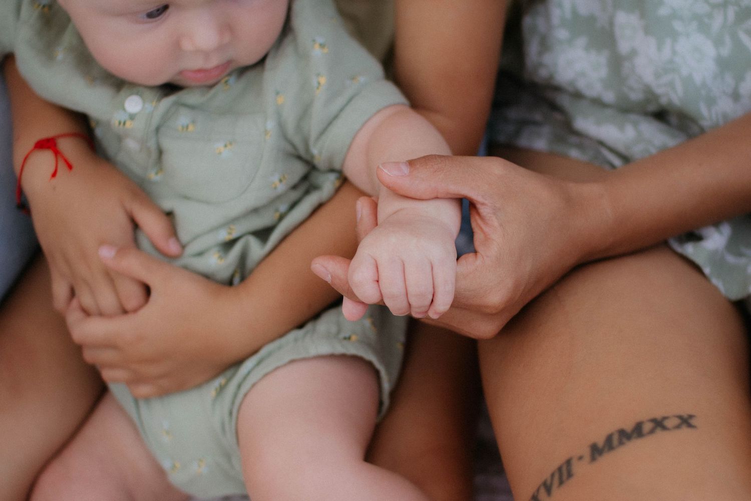Close up of small baby feet and hands being gently held by adult hands with visible tattoo.