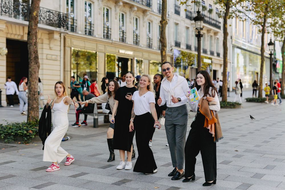 Group of stylish young people posing and taking selfies on a sunny Parisian boulevard.