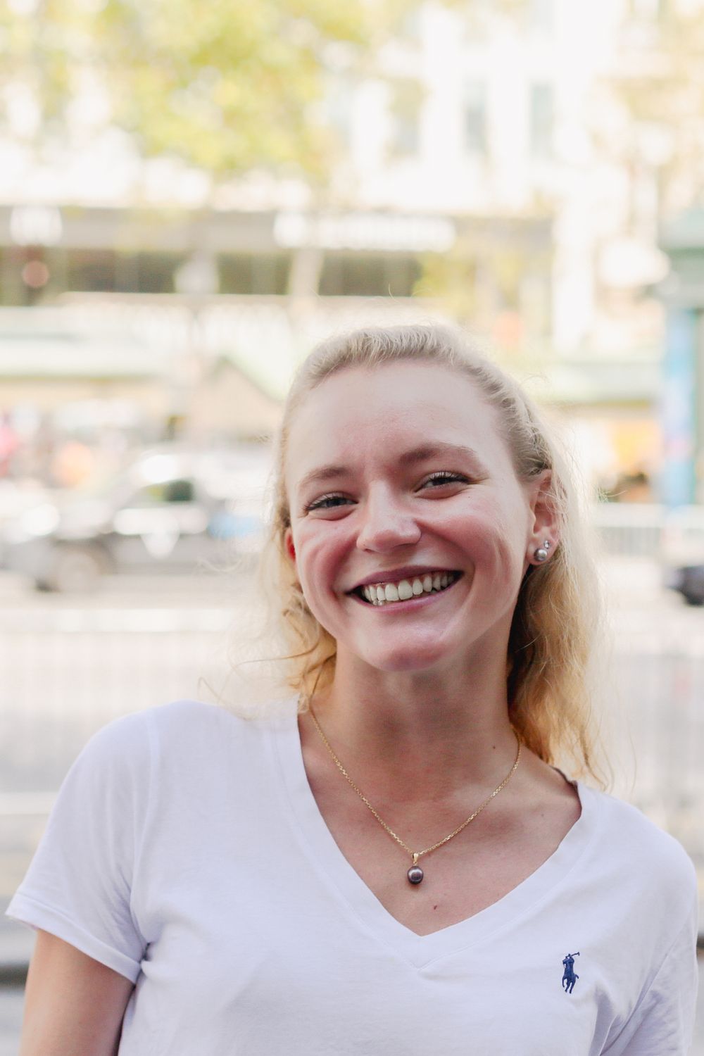 Smiling blonde woman in white Ralph Lauren t-shirt outdoors in urban setting.