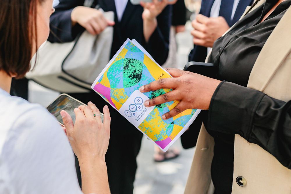 Hands exchanging colorful event program booklet at an outdoor gathering.