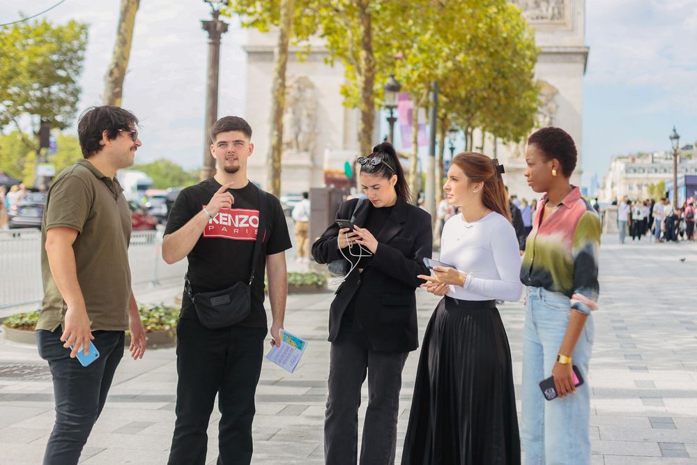 Diverse group of five young people conversing near the Arc de Triomphe in Paris.